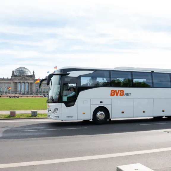 Ein BVB.net Reisebus fährt im Vordergrund auf der Straße, im Hintergrund der Reichstag in Berlin.