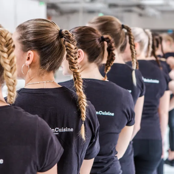 Mehrere Frauen mit geflochtenen Zöpfen stehen in einer Reihe, schwarze Shirts