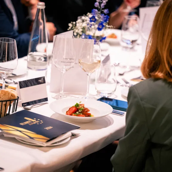Frau sitzt an festlich gedecktem Tisch mit Brot, Wein und Menükarte.