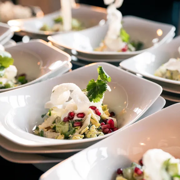 Mehrere Schalen mit Salat, Granatapfelkernen und einem Klecks Sahne, stilvoll angerichtet.