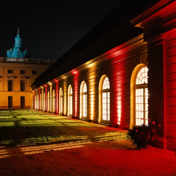Historisches Gebäude bei Nacht, bunt mit roten und gelben Lichtern beleuchtet.