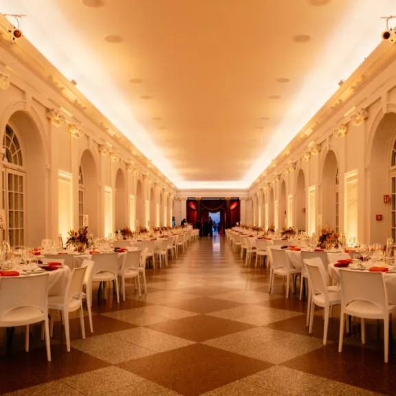 Elegant eingedeckter Festsaal mit weißen Stühlen und warmem Licht.