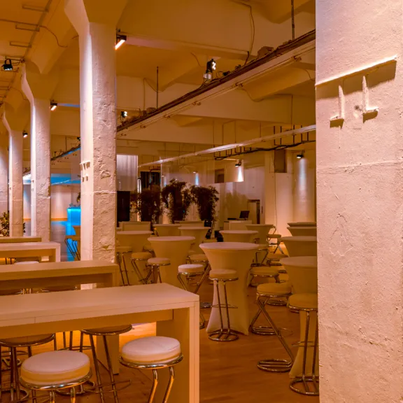 Modernes Restaurant mit hohen Decken, Holztischen und Barhockern, warm beleuchtet.