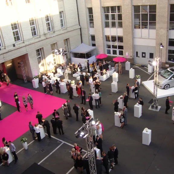 Hofevent mit vielen Menschen, Stehtischen, pinkem Teppich und einem ausgestellten Auto.