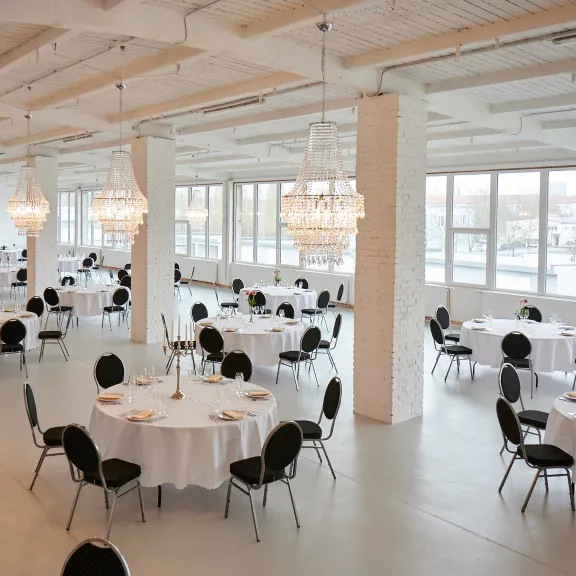 Großer, heller Festsaal mit runden, gedeckten Tischen und Kronleuchtern.