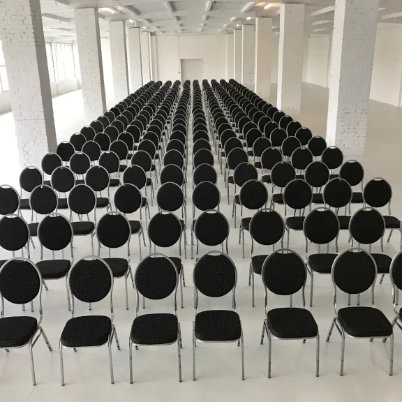 Viele Reihen schwarzer Stühle in einem großen, hellen Saal.