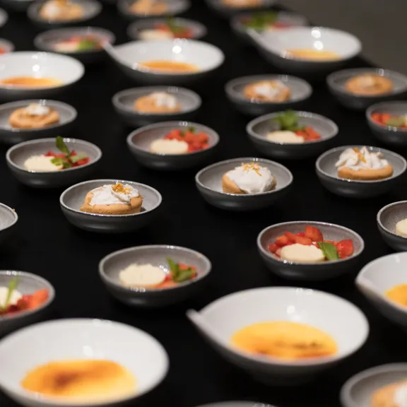 Viele kleine Dessertschälchen auf schwarzem Tisch, abwechslungsreich angerichtet.