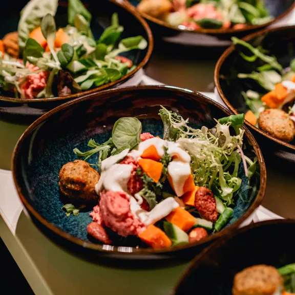 Mehrere Schalen mit bunter Gemüsesalat und Falafel auf einem Tisch.