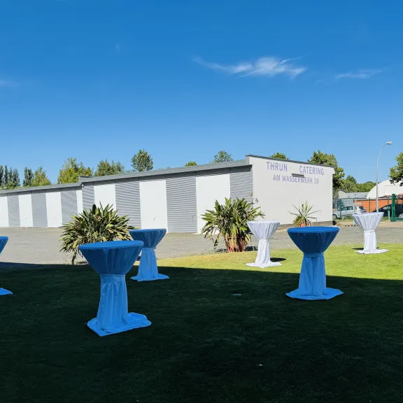 Stehtische mit weißen Hussen im Freien auf Rasen, Gebäude im Hintergrund