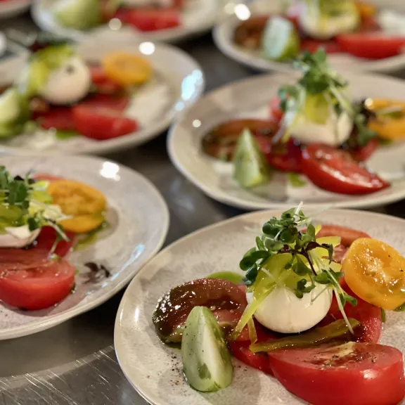 Mehrere Teller mit Caprese-Salat aus bunten Tomaten, Mozzarella und frischen Kräutern.