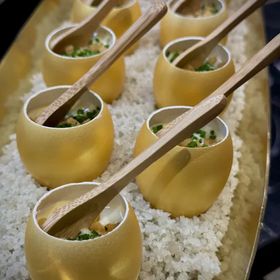 Kleine goldene Schalen mit Löffeln, serviert auf Reis, gefüllt mit Speise und Kräutern.