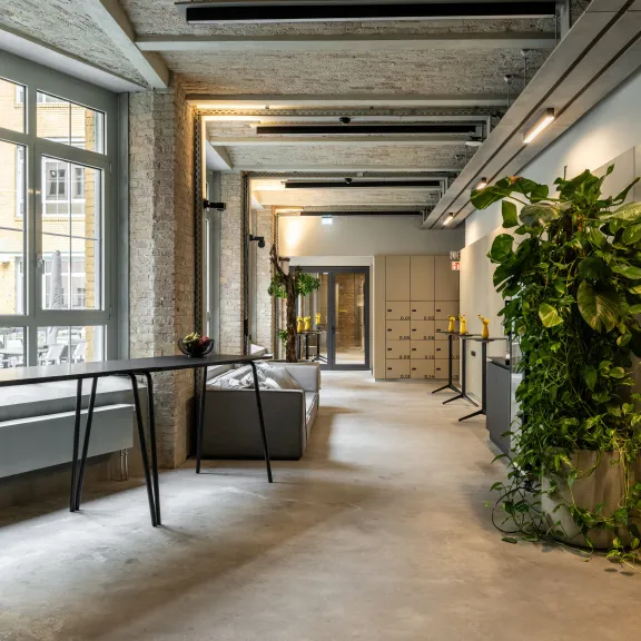 Heller Büroflur mit Pflanzen, Sitzgelegenheiten und großen Fenstern.