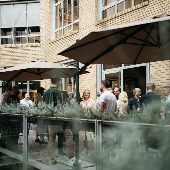 Menschen unterhalten sich im Innenhof mit Sonnenschirmen, umgeben von Backsteinwänden.