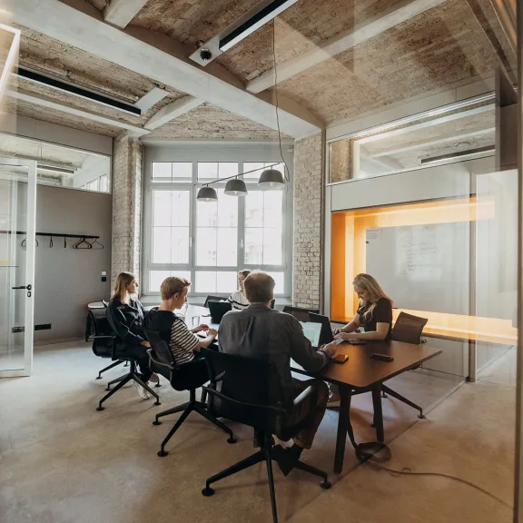 Vier Personen sitzen an einem Tisch in einem modernen Büro mit großen Fenstern.