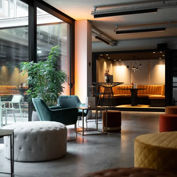 Heller, moderner Loungebereich mit großen Fenstern, Pflanzen und gemütlichen Sitzgelegenheiten.