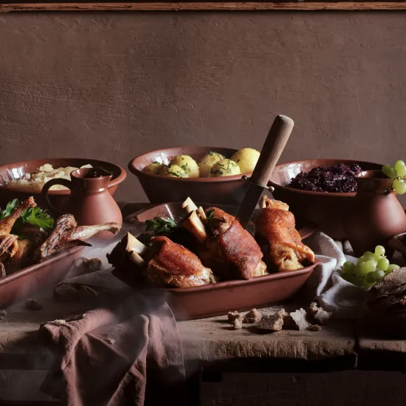 Rustikaler Tisch mit Braten, Kartoffeln, Rotkohl und frischem Brot.