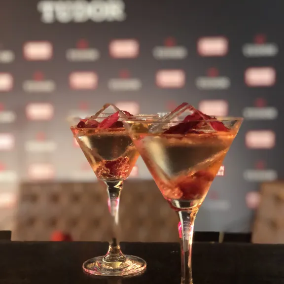 Zwei Cocktails mit Eis und Früchten vor unscharfem Hintergrund mit Markenlogo.