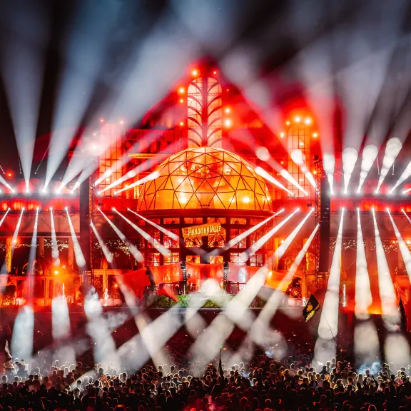 Große Bühne mit roten Lichtern und Laserstrahlen bei einem Musikfestival, Menschenmenge davor.