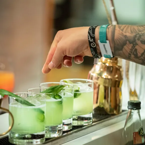 Hand mit Tattoos dekoriert grüne Cocktails an einer Bar.
