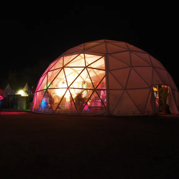 Beleuchtetes Kuppelzelt bei Nacht, bunte Lichter im Inneren, dunkle Umgebung.