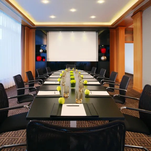 Moderner Konferenzraum mit langem Tisch, Stühlen und großer Leinwand vorne.