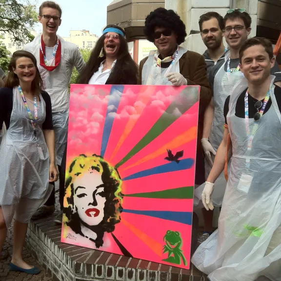 Gruppe von Menschen mit buntem Pop-Art-Gemälde, alle tragen weiße Schutzschürzen.