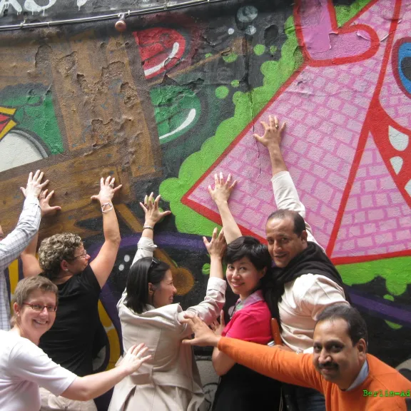 Gruppe fröhlicher Menschen posiert vor bunter Graffiti-Wand.