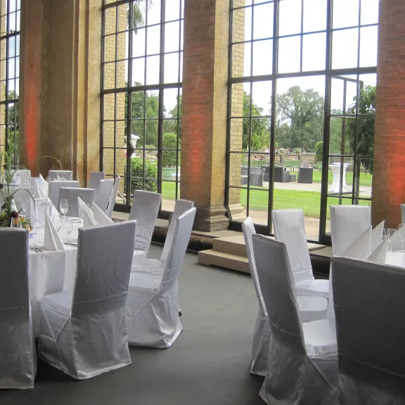 Elegant banquet tables with white chairs set by large windows overlooking a garden.