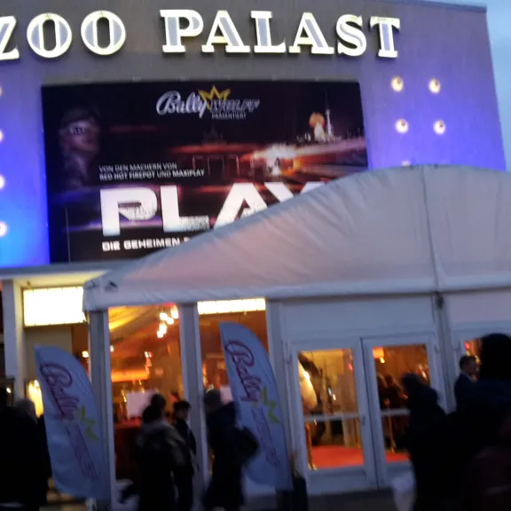 Kinoeingang Zoo Palast mit beleuchtetem Werbeplakat und wartenden Menschen.