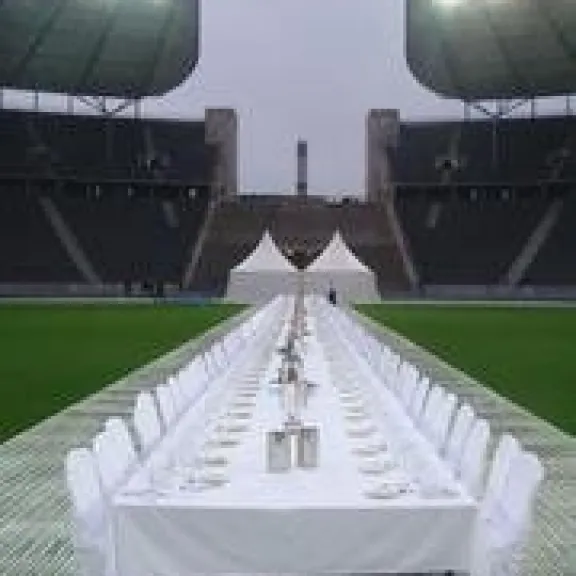 Lange, festlich gedeckte Tafel im Stadion, Scheinwerfer leuchten, leere Stühle.