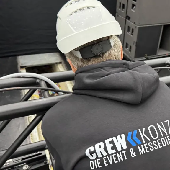 Mann mit Helm und CREWKONZEPT-Pullover arbeitet auf einer Bühne.