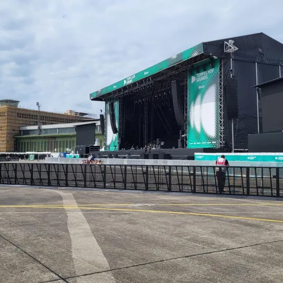 Leere Open-Air-Konzertbühne mit grünem Banner und Absperrungen vor der Bühne.