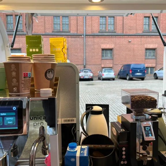 Kaffeemaschine und Pappbecher in einem mobilen Café, Blick nach draußen auf parkende Autos.