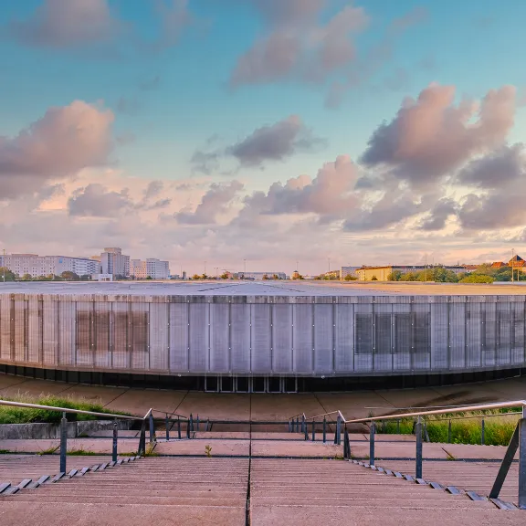 Rundes, modernes Gebäude bei Sonnenuntergang, vorne Treppen und Handlauf.