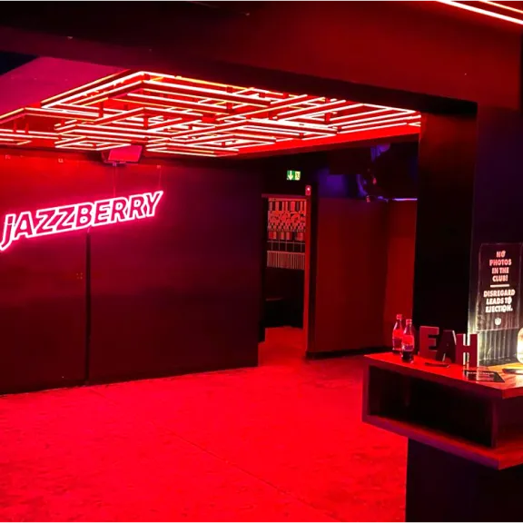 Bar mit neonroter Beleuchtung, moderner Einrichtung und leuchtendem Schriftzug an der Wand.