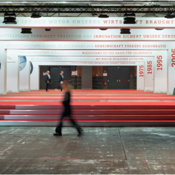 Person geht durch eine modern gestaltete Ausstellungshalle mit roten Stufen und weißen Wänden.