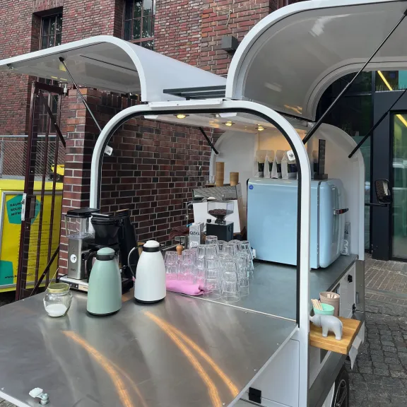 Moderner Kaffeestand mit zwei Thermoskannen vor roter Backsteinwand.