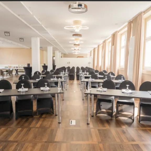 Heller Konferenzraum mit langen Tischen, Stühlen und großen Fenstern.