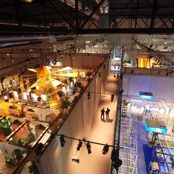 Große Messehalle mit bunten Messeständen und wenigen Menschen auf den Gängen.