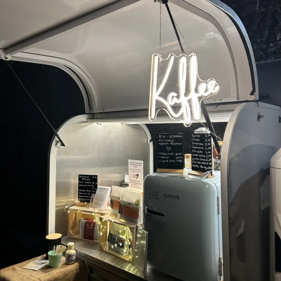 Leuchtendes Neon-Schild mit Herz, Getränke und Kaffeemaschine in einem mobilen Stand.
