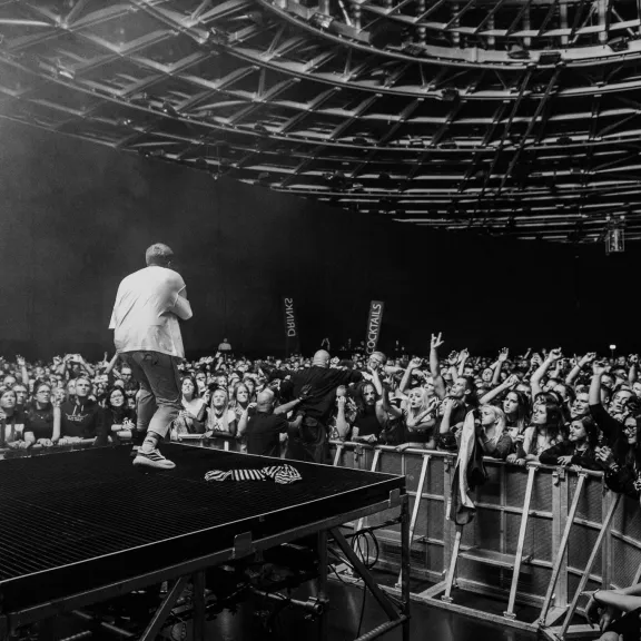 Schwarz-weiß-Foto: Künstler auf Bühne, jubelndes Publikum in einer Konzertarena.