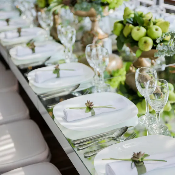 Festlich gedeckter Tisch mit weißen Tellern, Gläsern und grüner Dekoration.