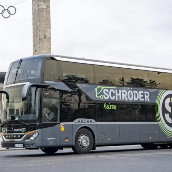 (1)	Moderner grauer Doppeldecker-Reisebus mit der Aufschrift „Schröder Reisen“ steht vor dem Berliner Olympiastadion; im Hintergrund sind die beiden Türme mit den Olympischen Ringen zu sehen.