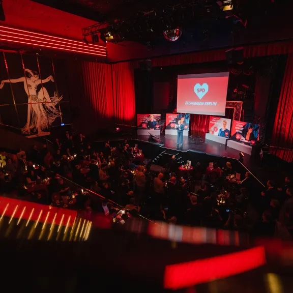 Bühne mit rotem Licht, Publikum sitzt, Herzsymbol auf Leinwand im Hintergrund.