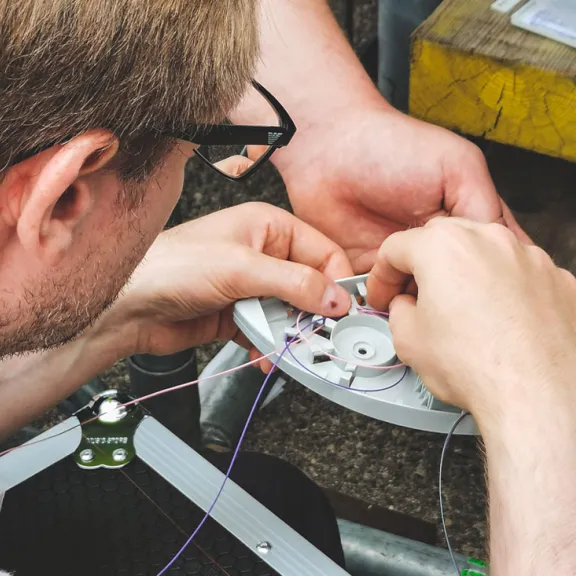 Mann repariert eine kleine mechanische Vorrichtung mit feinen Drähten.