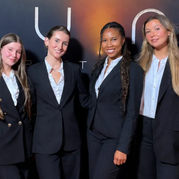 Vier lächelnde Messehostessen in eleganten schwarzen Business-Anzügen auf einem Corporate Event. Professionelles Promotion-Personalvon VPeople GmbH