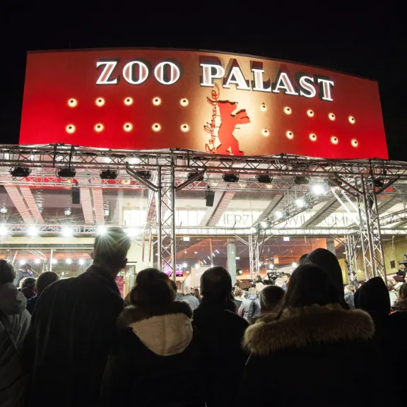 Menschenmenge vor dem beleuchteten Kino Zoo Palast bei Nacht.