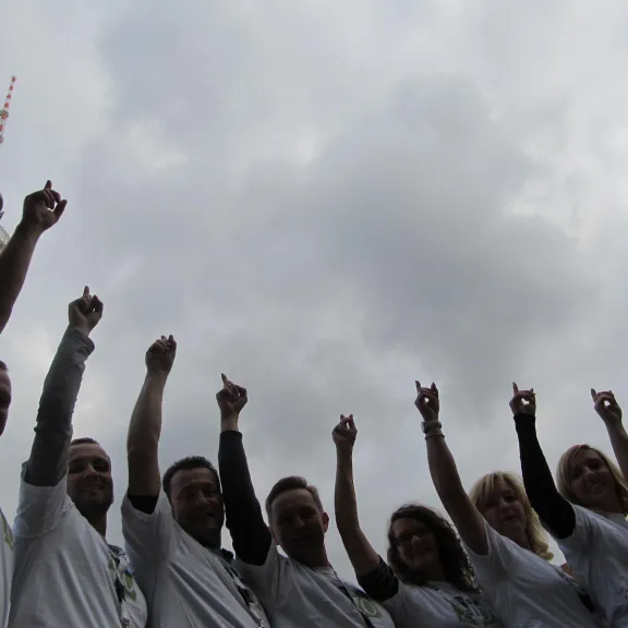 Gruppe von Menschen zeigt nach oben, Fernsehturm im Hintergrund, bewölkter Himmel.