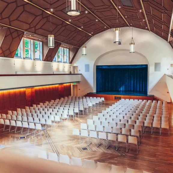 Festsaal Blick von der Empore in den Saal mit Reihenbestuhlung und Bühne mit blauem Vorhang