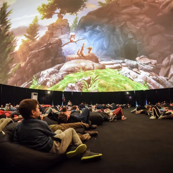 Menschen liegen auf Sitzsäcken und schauen eine Projektion in einer Kuppel an.
